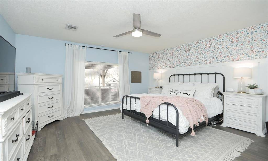 A bright and inviting primary bedroom featuring a decorative floral accent, a large window overlooking the backyard, and a modern ceiling fan.
