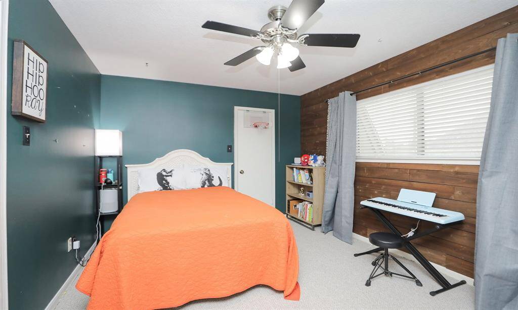 An upstairs bedroom features warm walls, a wood accent wall, and a ceiling fan.