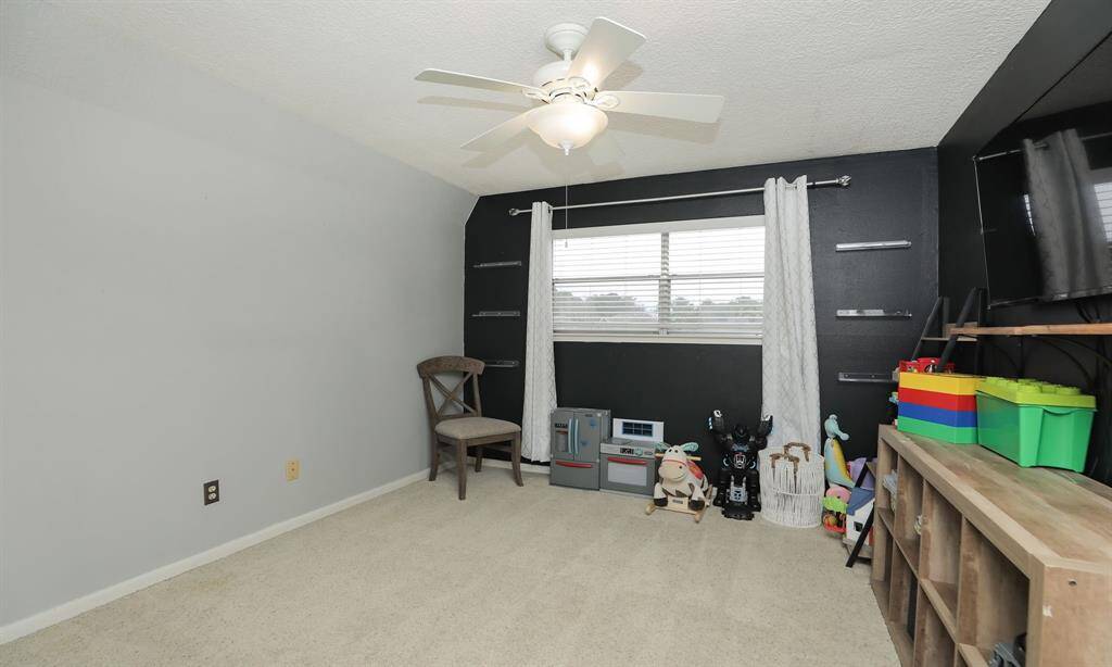 The third bedroom upstairs has neutral walls with a contrasting dark accent, carpeted flooring, and a ceiling fan, perfect for a playroom or home office.