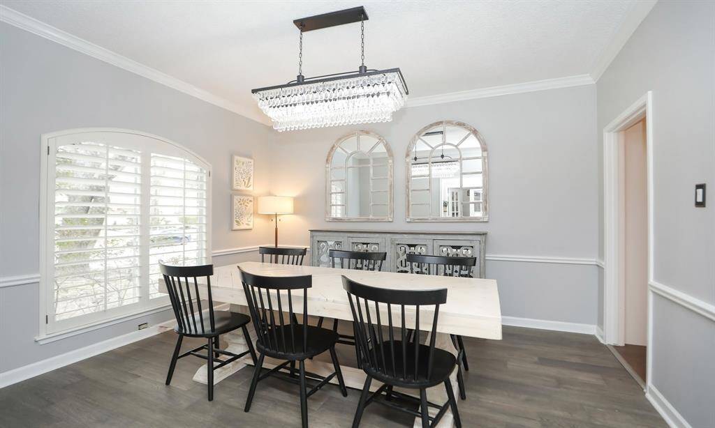This dining room features a modern chandelier. Large windows with plantation shutters allow natural light as well as privacy.