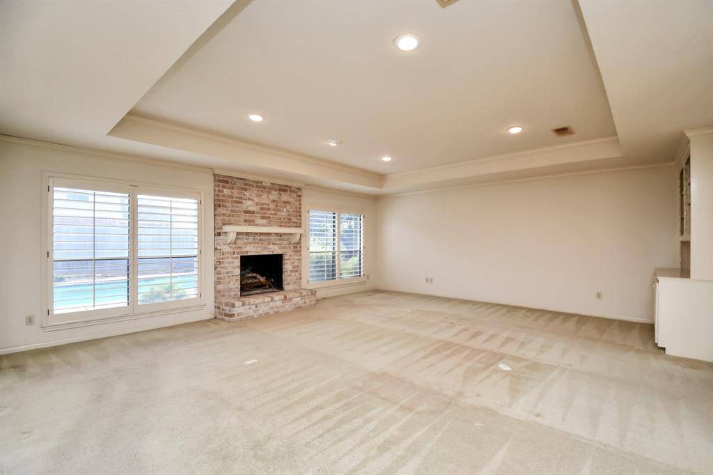 Spacious living room with tray ceiling, custom built in shelves, brick fireplace and picture windows overlooking peaceful backyard.