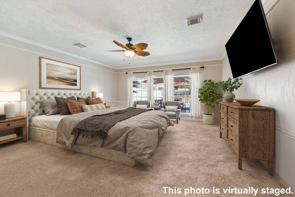 This expansive first-floor primary bedroom boasts large windows overlooking the backyard, filling the space with natural light. The neutral color palette, elegant trim work, and carpeting create a cozy atmosphere. There is  ample space allowing for a comfortable seating area or additional furnishings.