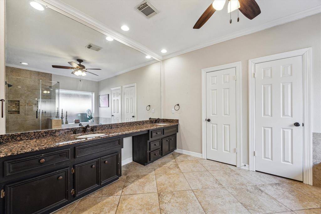 This primary bathroom offers dual vanities with granite countertops, a vanity, and ample cabinet storage. The double closets provide plenty of space for organization.