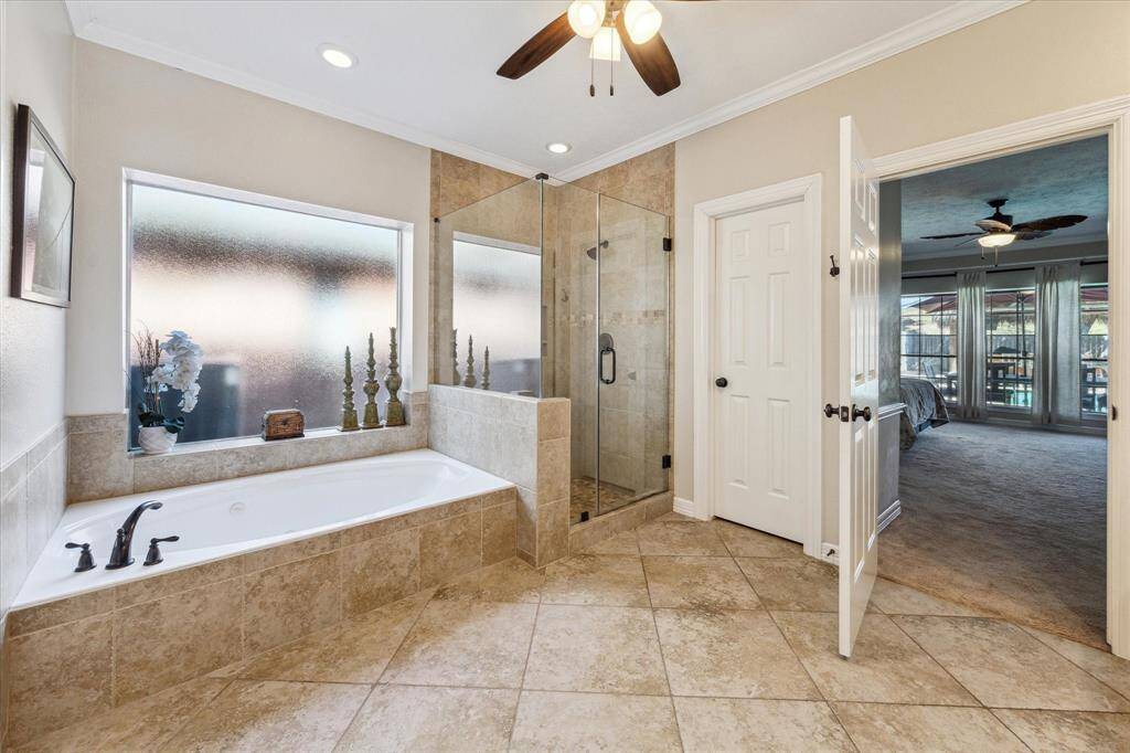 This primary bathroom offers a serene retreat, featuring a soothing jetted tub beneath a large frosted window that fills the space with natural light while ensuring privacy. The glass-enclosed walk-in shower boasts intricate tilework and built-in niches for added convenience. With recessed lighting and a neutral color palette, this spa-like space exudes warmth and relaxation.