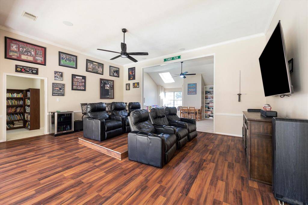 This stylish media room located at the top of the stairs is designed for the ultimate viewing experience, featuring tiered flooring for seating, laminate wood flooring, and a wall-mounts for tv setup. An open flow to the game room with built-in shelving and skylights makes this space perfect for movie nights, gaming, and entertaining.