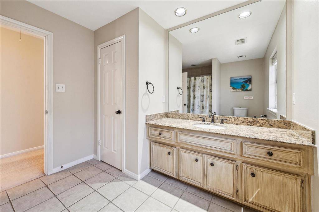 This upstairs bathroom shared by two bedrooms features a granite-topped vanity with ample storage, in addition to the linen closet, a large mirror, recessed lighting for a bright and open feel and tile flooring.  A window allows natural light to enhance the space.