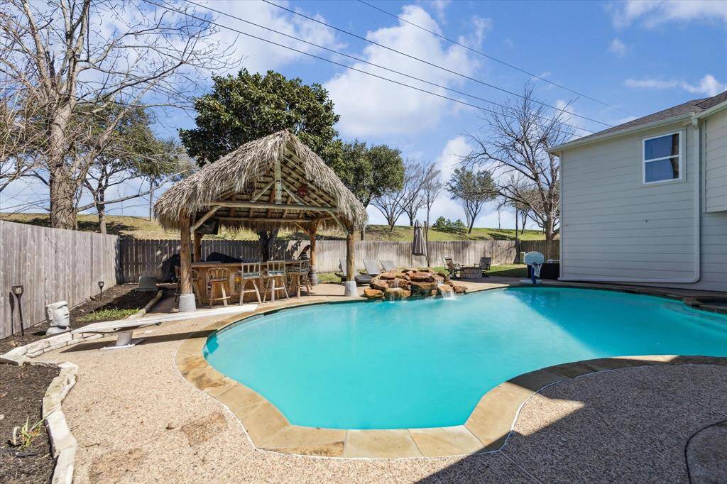 An additional view of the relaxing backyard pool area, custom built palapa and outdoor bar area. The rock waterfall was added the pool in 2019.