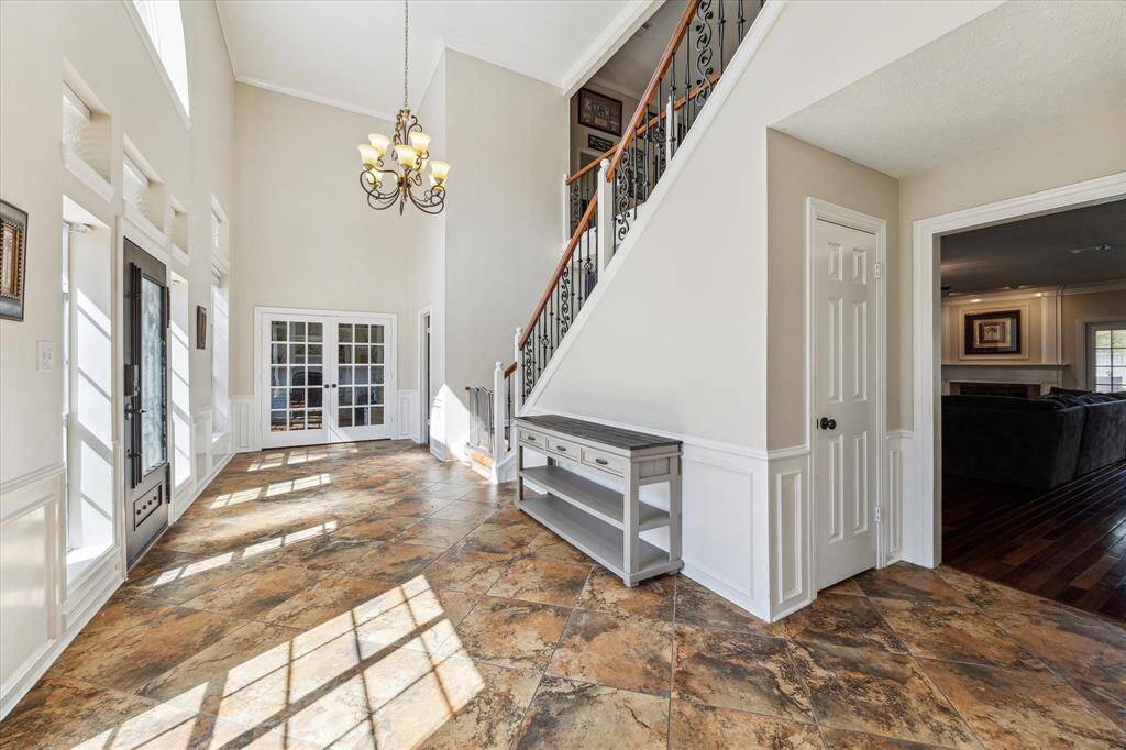 Enter this stunning two-story foyer, where soaring ceilings, abundant natural light, and a striking wrought-iron staircase create a grand first impression. The open layout seamlessly connects to the formal dining room, perfect for hosting gatherings. Elegant **tile flooring, wainscoting, and a statement chandelier** add a touch of sophistication. Designed for both style and function, this inviting entryway flows effortlessly into the main living areas and home office.