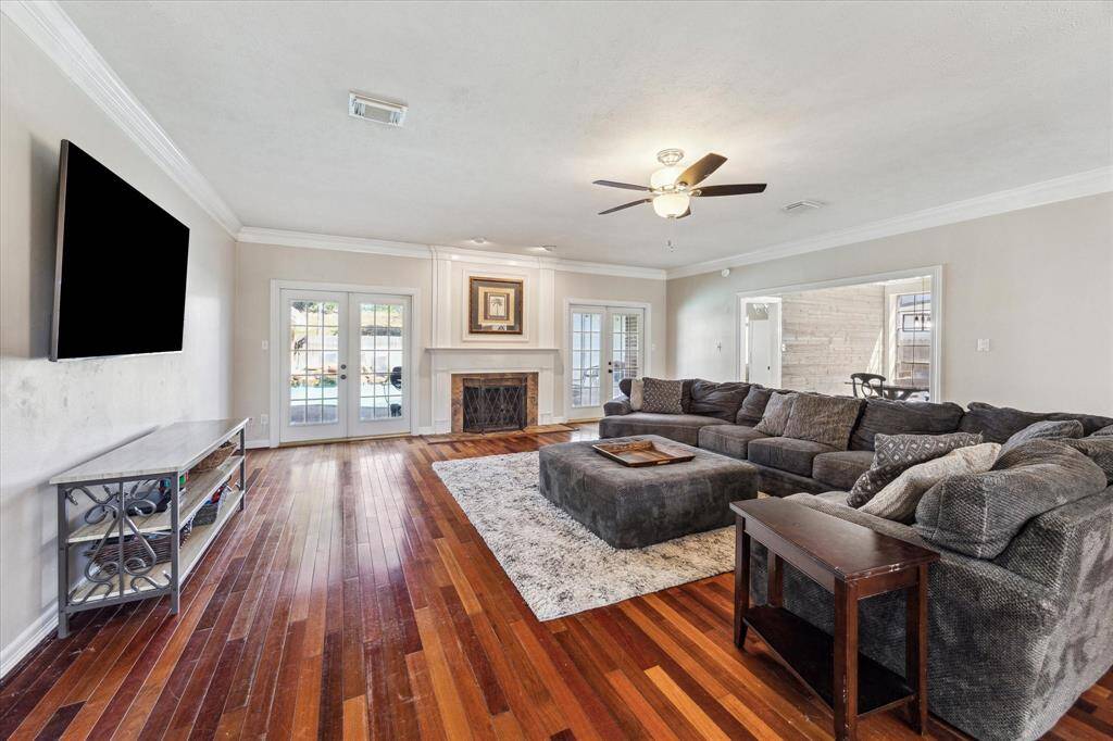 This inviting living room features warm hardwood flooring, elegant crown molding, and a cozy fireplace. French doors on either side of the gas log fireplace, with a natural gas insert, lead directly to the backyard, offering a seamless indoor-outdoor living experience. Perfect for relaxing or entertaining, this space is the heart of the home!