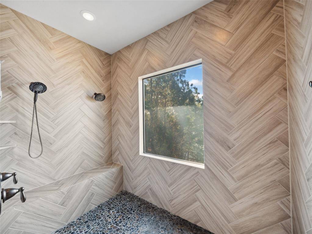 PRIMARY SHOWER Gorgeous finishes and lake and tree views. Incudes a huge bench, pretty river pebble tile with more of the striking herringbone design.