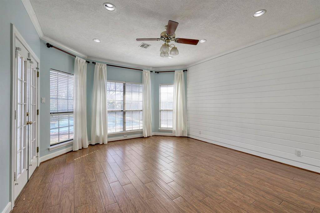 This room features large windows to allow plenty of natural light. It has wood-look flooring, a ceiling fan, and French doors, offering a bright and airy space.