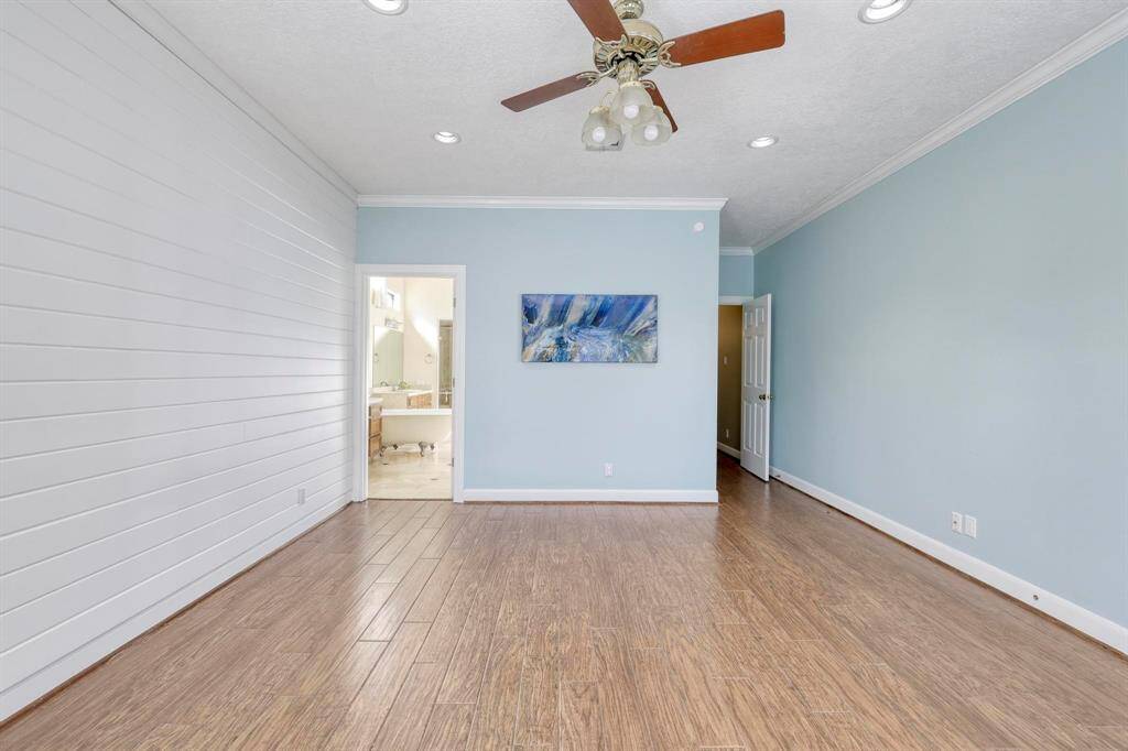 This room features wood flooring, light blue walls, and a white shiplap accent wall. It has recessed lighting, a ceiling fan, and an open doorway leading to a bathroom.