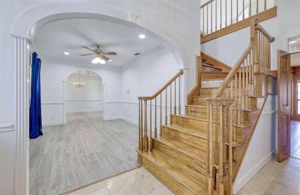 This photo showcases a bright entryway with a wooden staircase leading to the upper floor. The space features elegant archways, light flooring, and a ceiling fan, offering an inviting and open feel.