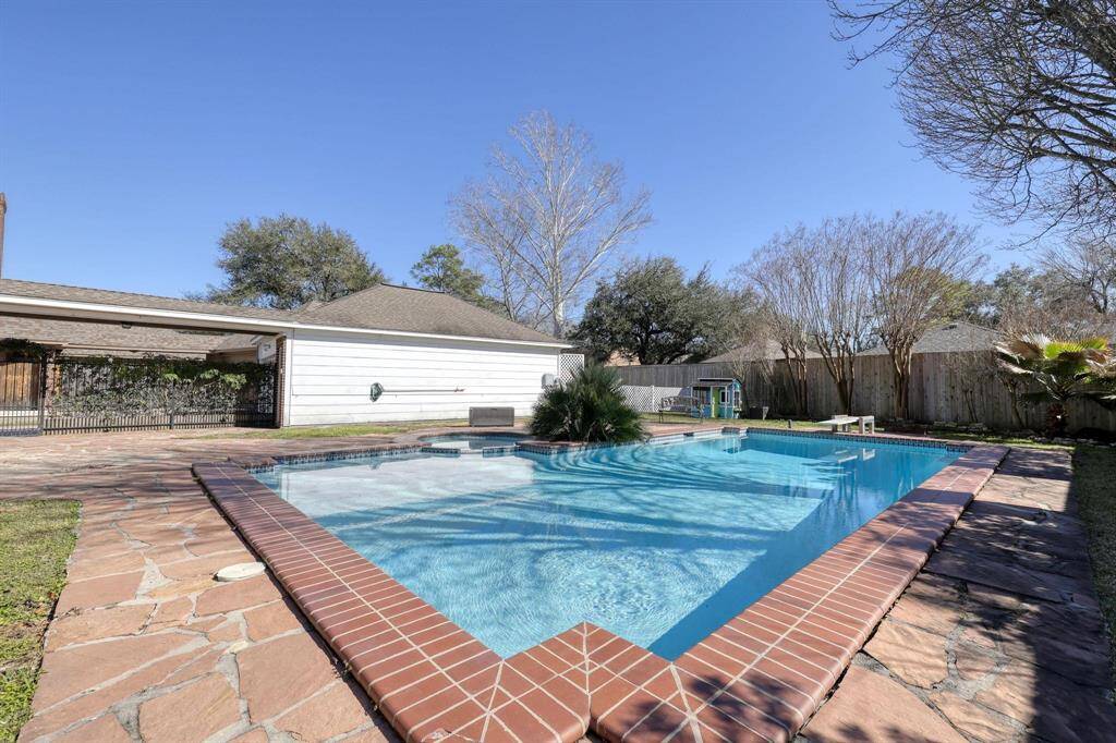 This backyard features a spacious in-ground pool with a stone deck, surrounded by mature trees and a privacy fence, creating a serene outdoor retreat.