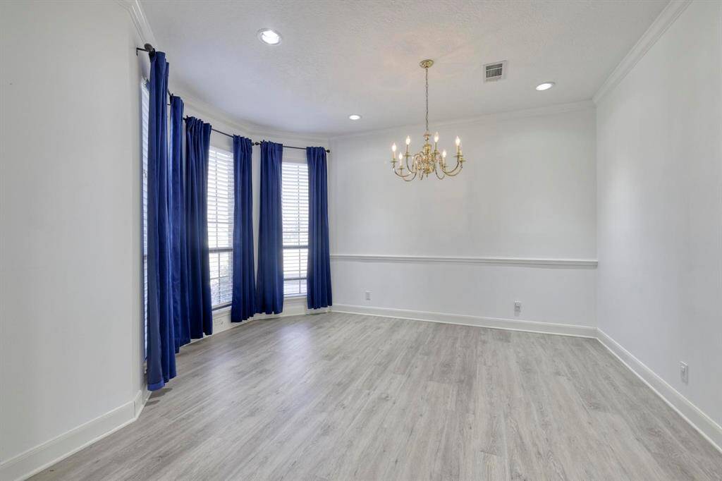 This room features light wood flooring, a chandelier, and a large window with blue curtains, creating a bright and elegant space.