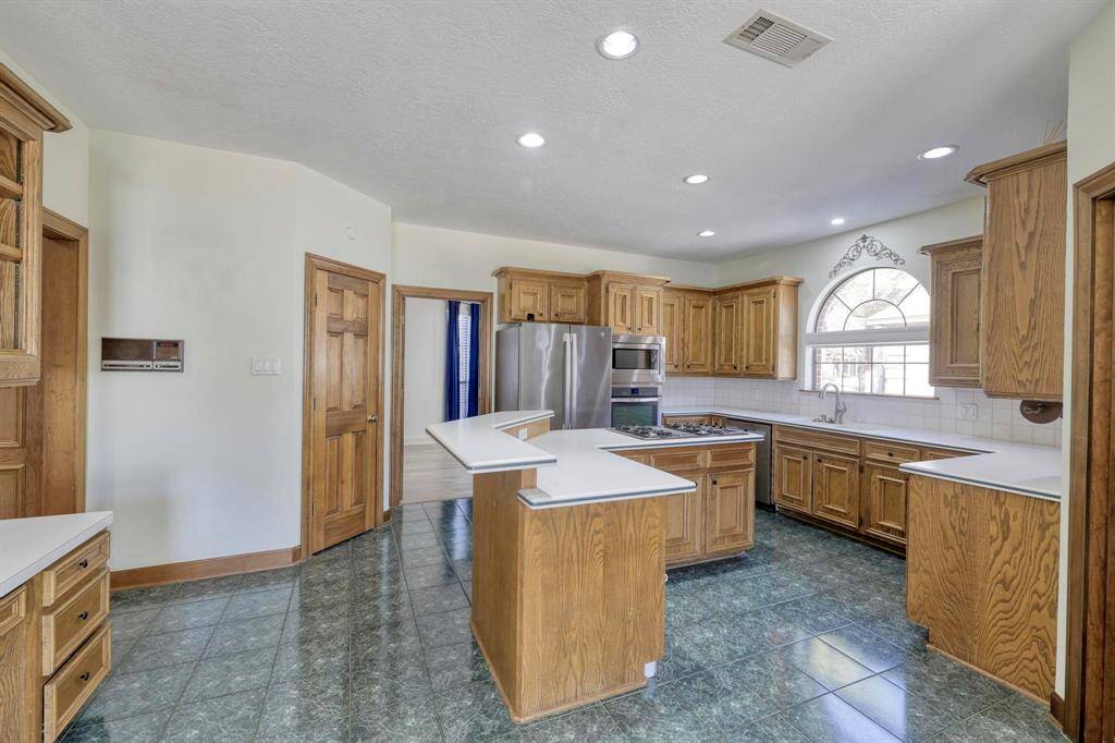 Spacious kitchen with ample wooden cabinetry, a central island, and modern stainless steel appliances. Features large windows for natural light and recessed ceiling lights, creating a bright and inviting atmosphere.