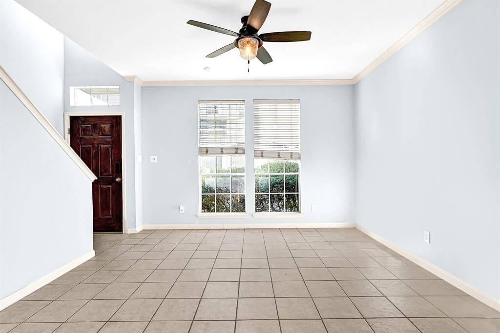 Bright and inviting living room with large windows, stylish tile flooring, and a ceiling fan for comfort. Perfect for relaxing or entertaining.