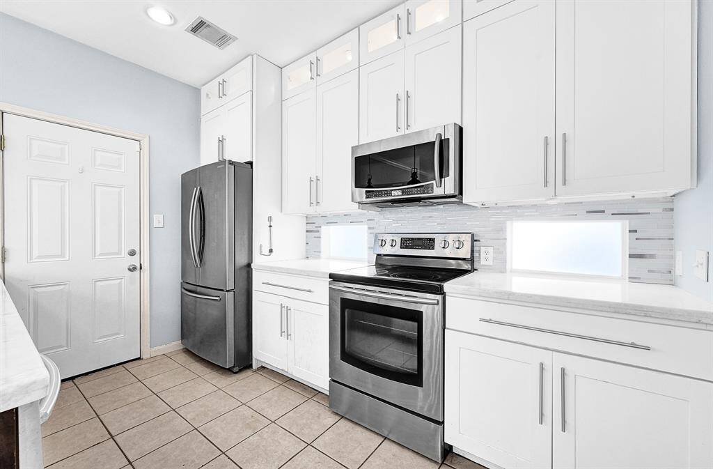 Modern kitchen with sleek stainless steel appliances, ample white cabinetry, and stylish tile backsplash.