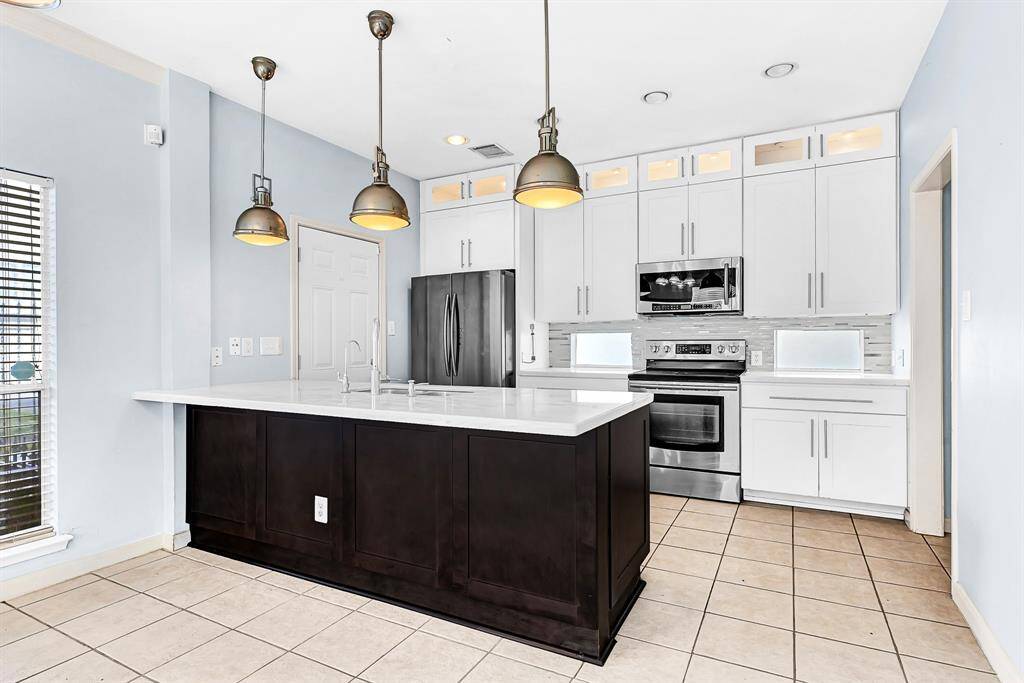 This modern kitchen features sleek white cabinetry, stainless steel appliances, and a central island with pendant lighting. The tile floor complements the contemporary design, creating a bright and inviting space.