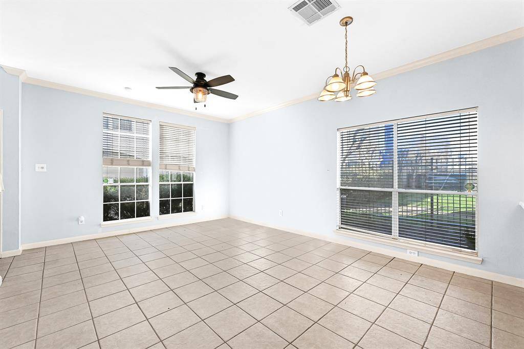This bright, spacious room features light blue walls, large windows with blinds, tiled flooring, a ceiling fan, and a chandelier, offering a versatile space for dining or living.