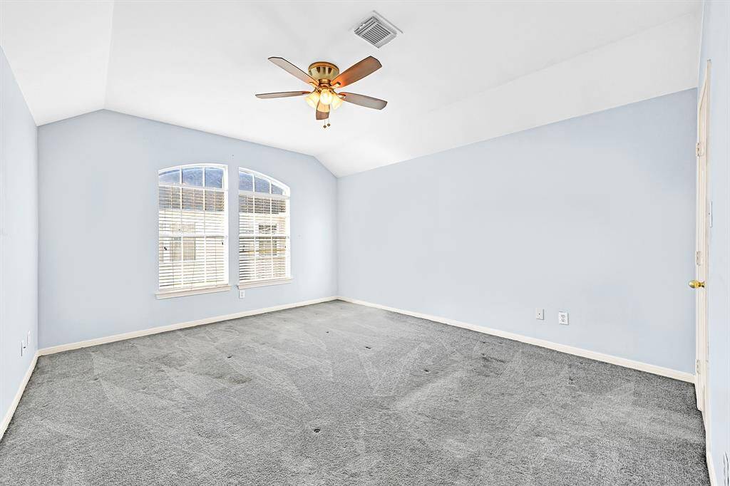 Spacious master bedroom with vaulted ceilings, large windows for natural light, and a stylish ceiling fan. Perfect for relaxation and comfort.