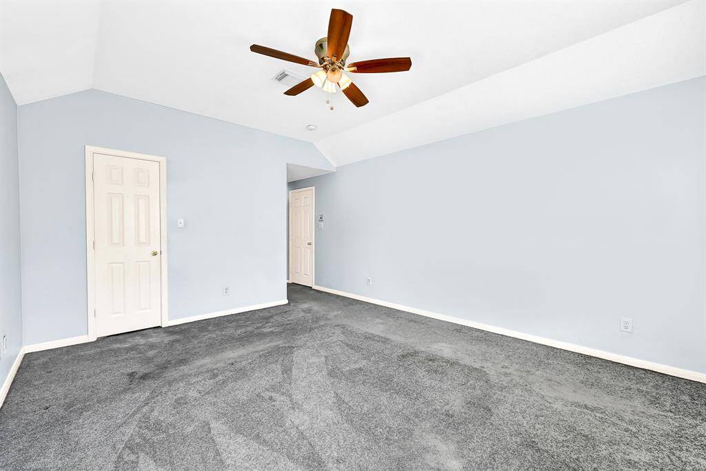 This room features soft blue walls, gray carpeting, and a ceiling fan. It has a clean, spacious feel with two white doors and recessed lighting, ideal for a bedroom or office space.