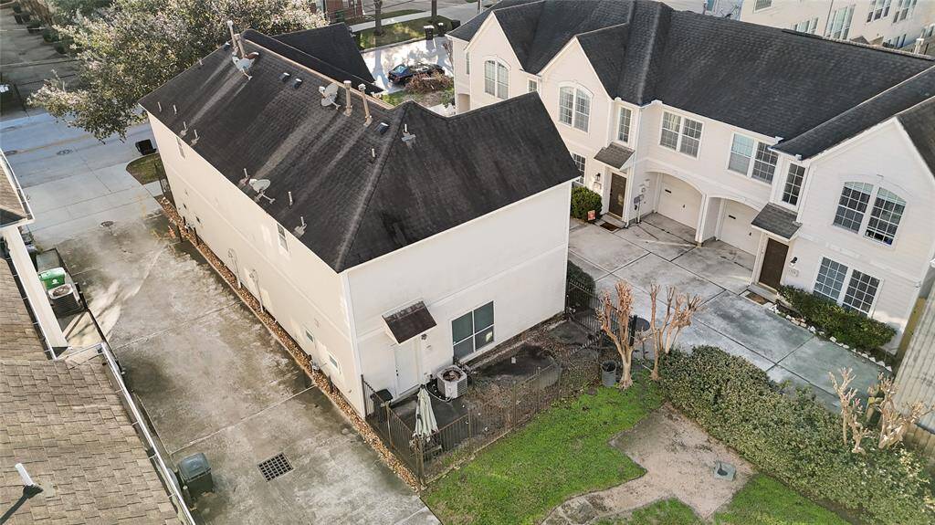 This aerial view showcases a townhouse with a dark roof, white exterior, and a paved driveway. It features a small grassy backyard and is part of a connected row of homes. The area appears well-maintained and residential.
