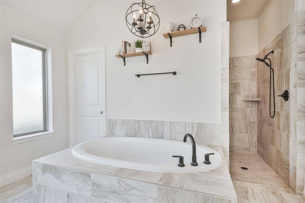 Soaking tub and chandelier are flanked by super shower and two walk-in closets.