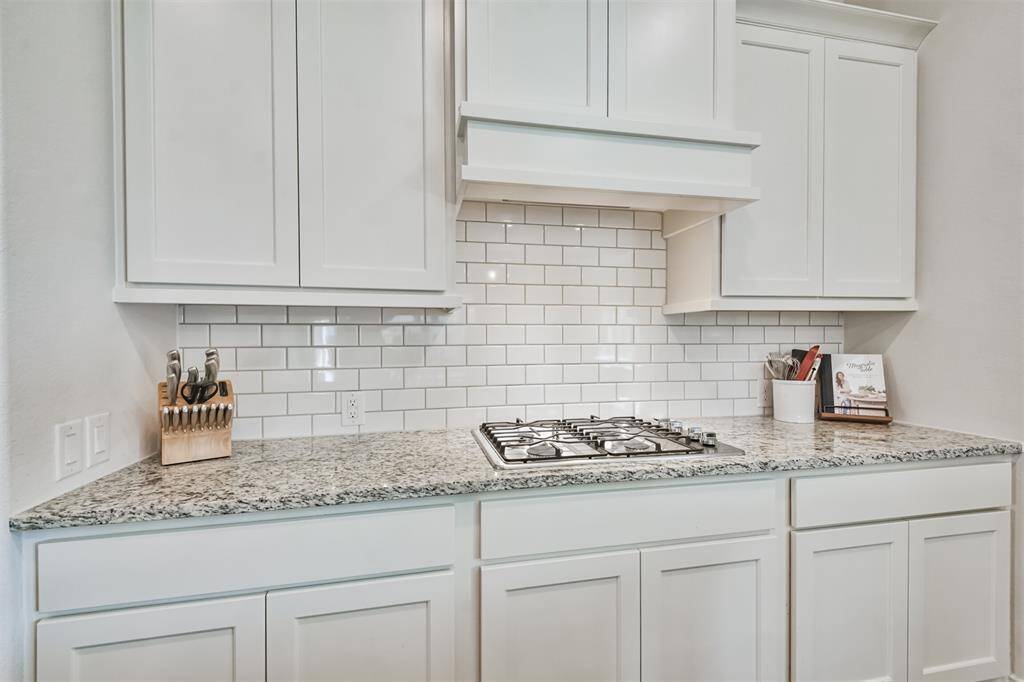 Gas cooktop, granite counters, subway tile backsplash and wrapped vent hood controlled by remote provide beauty and function.