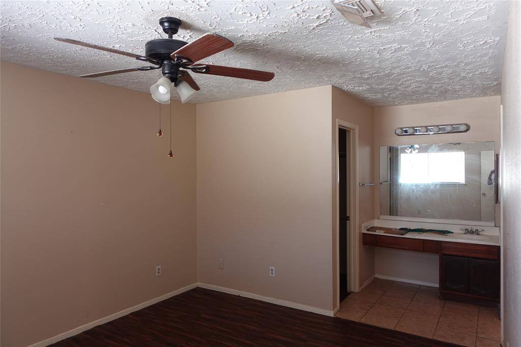 Spacious master bedroom featuring elegant laminate flooring, an en-suite vanity area, and a modern ceiling fan for ultimate comfort.