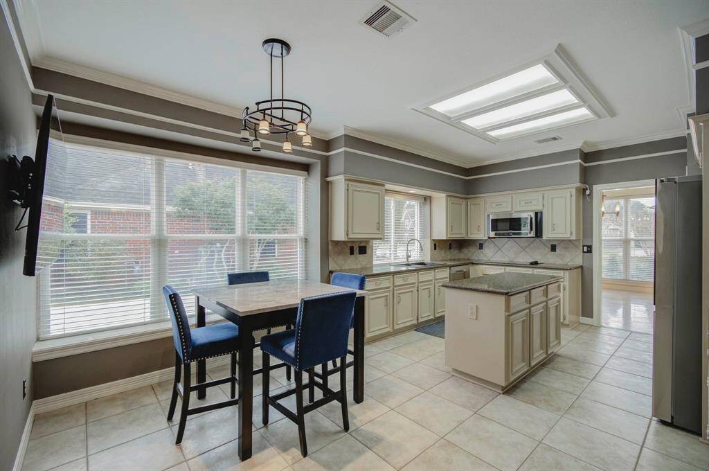 This bright kitchen features large windows, ample natural light, and modern lighting fixtures. It includes a cozy dining area, sleek granite countertops, and updated appliances, ideal for both cooking and entertaining.