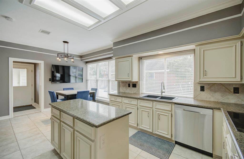 Bright kitchen with modern lighting, large windows, and abundant natural light. Features include granite countertops, cream-colored cabinetry, stainless steel appliances, and a cozy dining area. Ideal for both cooking and entertaining.