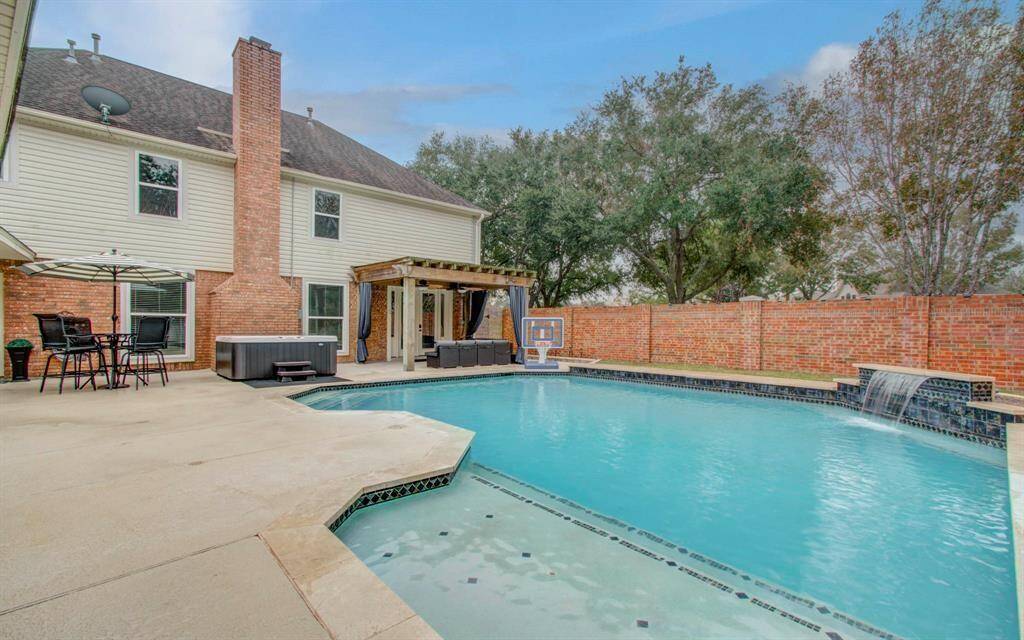 Spacious backyard featuring a large swimming pool with a waterfall feature, and a cozy covered patio area perfect for relaxation.