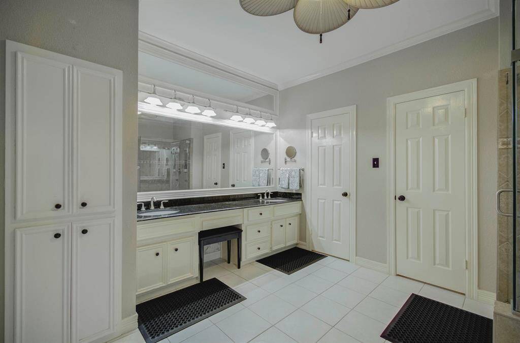 This spacious bathroom features dual sinks with a large mirror, ample cabinet storage, and modern lighting. The neutral tones and tile flooring create a clean, elegant look.