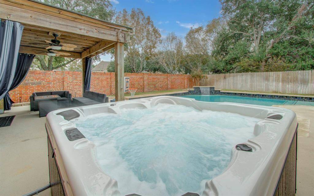 This outdoor space features a swimming pool with a waterfall feature, and a cozy covered patio with seating and ceiling fans, ideal for relaxation and entertaining.