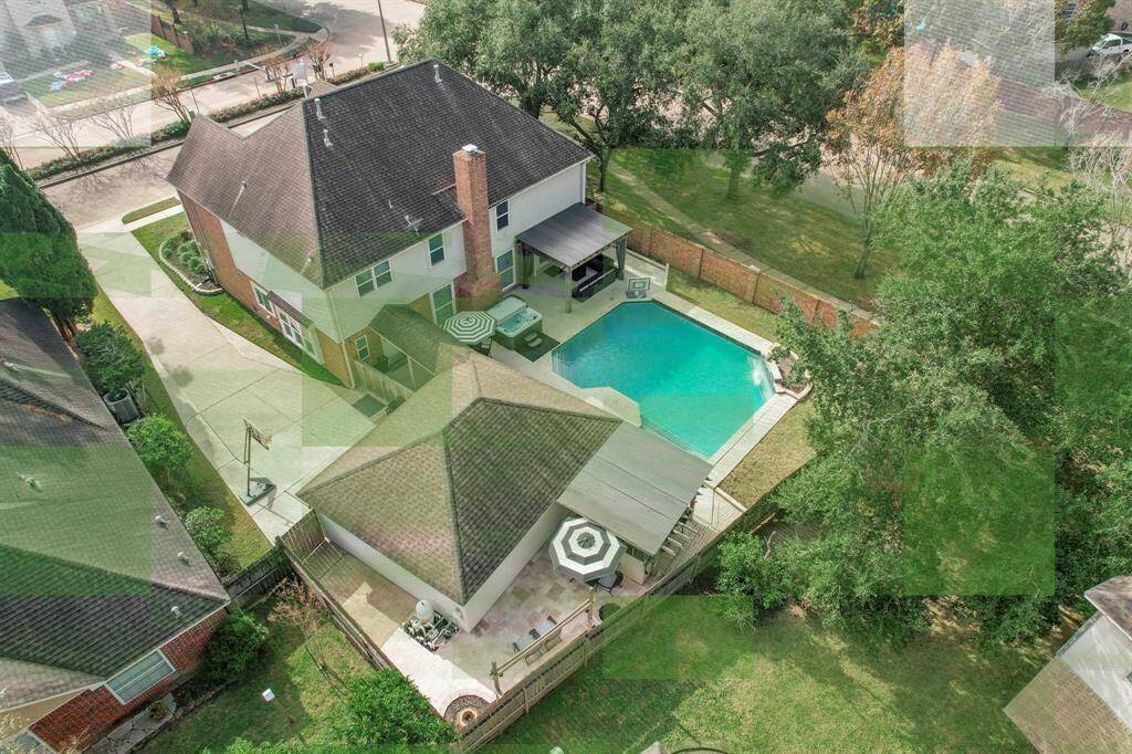 This aerial view showcases a spacious two-story home with a backyard featuring a swimming pool and a covered patio area. The property is bordered by a privacy fence and surrounded by mature trees, offering a private and serene outdoor space.