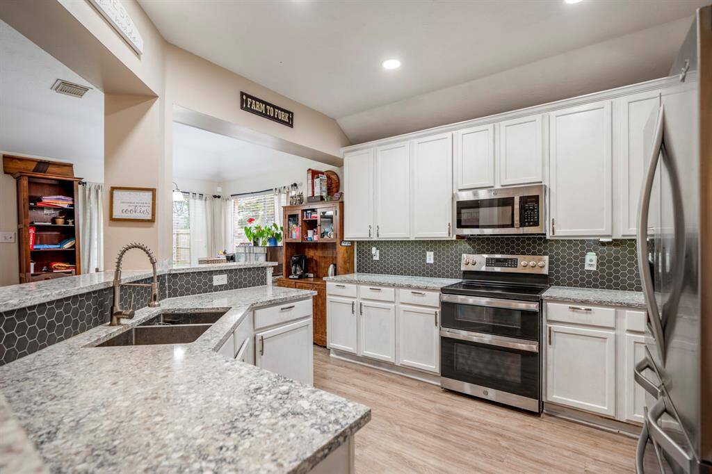 Entering the kitchen, you'll notice the gleaming quartz counters, decorative backsplash, under cabinet lighting, and a stainless steel appliance package, including a double basin sink with a pull-out faucet. The electric range features double ovens with a built-in microwave above, offering both style and functionality.