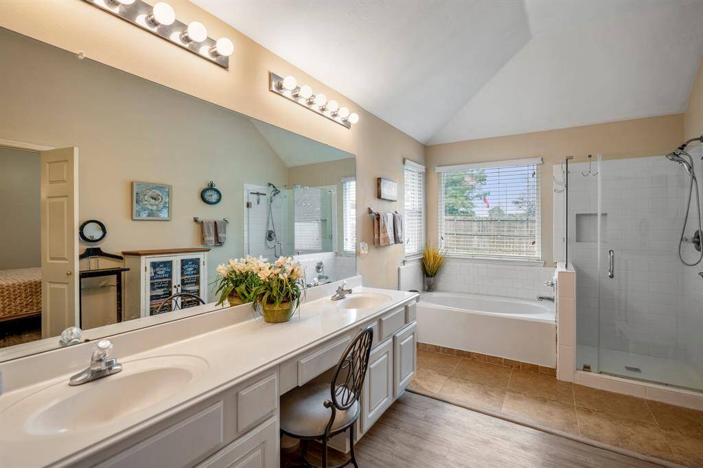 Moving into the primary bath, we get a closer look at the beautiful tile shower with a glass enclosure, as well as the separate tub with corner windows overhead, allowing natural light to brighten the space and create a serene atmosphere.