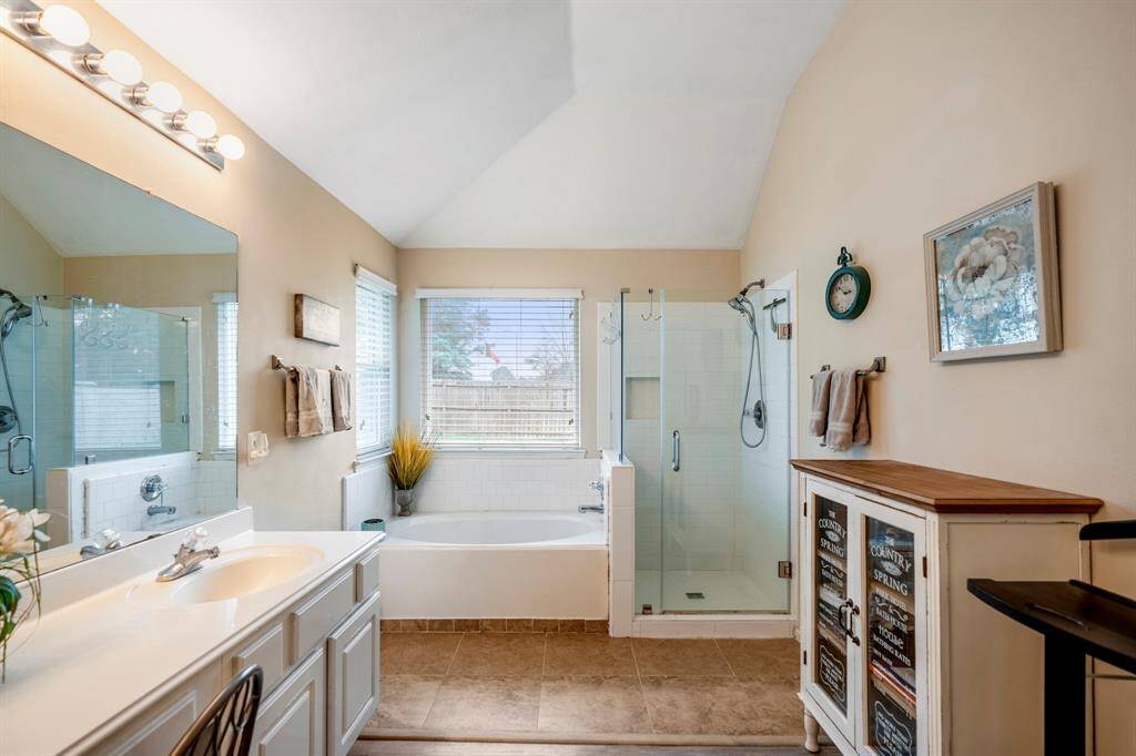 Another view of the primary bath, showcasing the tile shower with glass enclosure, separate tub with corner windows overhead, and dual sinks with a vanity area. The layout offers both functionality and relaxation, creating a tranquil retreat.