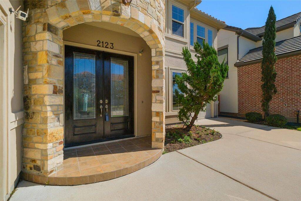 Welcome home to an inviting entryway that exudes sophistication and charm! This striking stone archway leads to an impressive set of double glass doors with intricate wrought iron detailing, setting the stage for the luxury that awaits inside. The beautifully tiled front porch adds warmth and refinement, creating the perfect first impression for guests. Step inside and experience the grandeur for yourself—your dream home starts here!