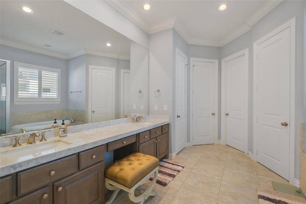 Indulge in elegance and comfort in this beautifully designed primary bathroom. Featuring a spacious dual vanity with stunning marble countertops, rich wood cabinetry, and a dedicated makeup area, this space offers both style and functionality. The oversized mirror enhances the room’s brightness, while recessed lighting and crown molding add a touch of sophistication.