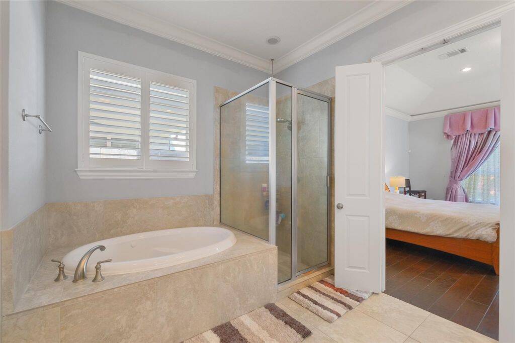 A large soaking tub and separate glass-enclosed shower provide the perfect retreat for relaxation. Natural light filters in through the shuttered window, creating a spa-like ambiance. With ample storage and multiple closets, organization is effortless in this serene sanctuary.Unwind in this luxurious bathroom—your personal oasis awaits!