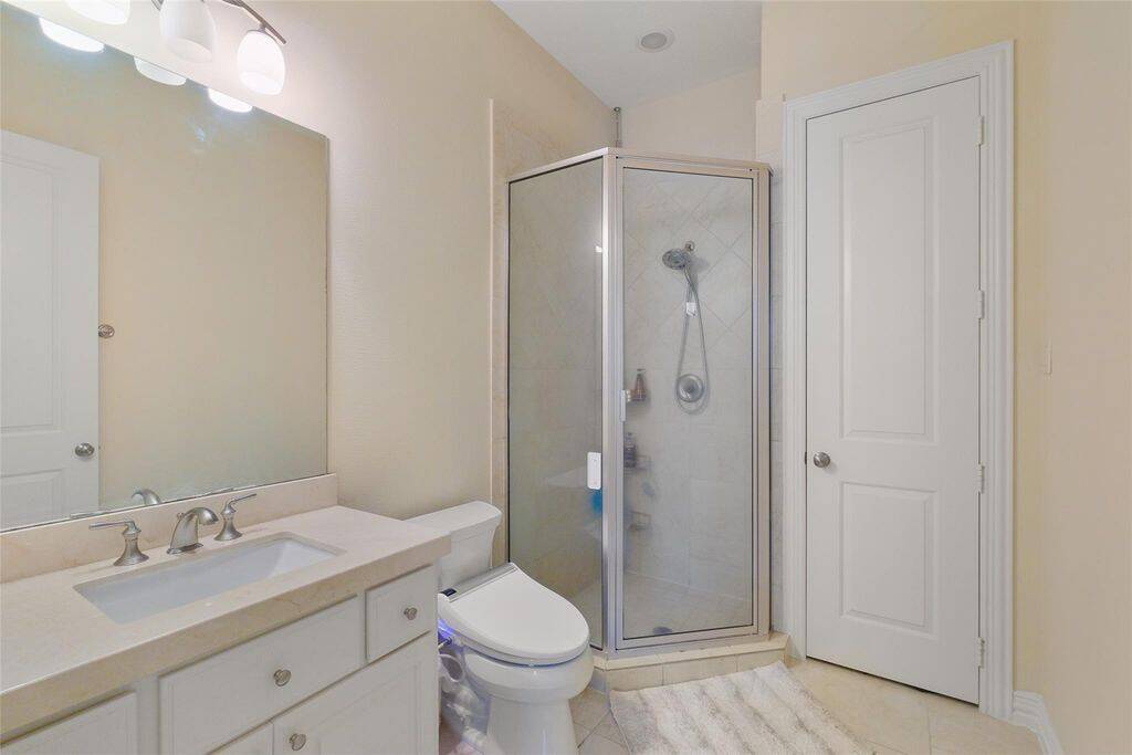 Designed for both convenience and elegance, this en-suite bathroom boasts a modern, functional layout. The glass-enclosed shower offers a sleek and refreshing experience, while the vanity provides ample storage to keep essentials neatly organized. A large mirror enhances the space, reflecting natural light for an airy and open feel.