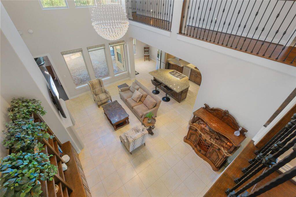 This stunning bird’s-eye view captures the grandeur of the home’s open-concept design, seamlessly connecting the living room, kitchen, and outdoor space. The soaring ceilings and expansive windows flood the area with natural light, creating an airy and inviting atmosphere.A dazzling chandelier serves as a striking centerpiece, while the wrought iron railing on the second-floor balcony adds an elegant architectural touch. From this vantage point, you can appreciate the home’s flowing layout!