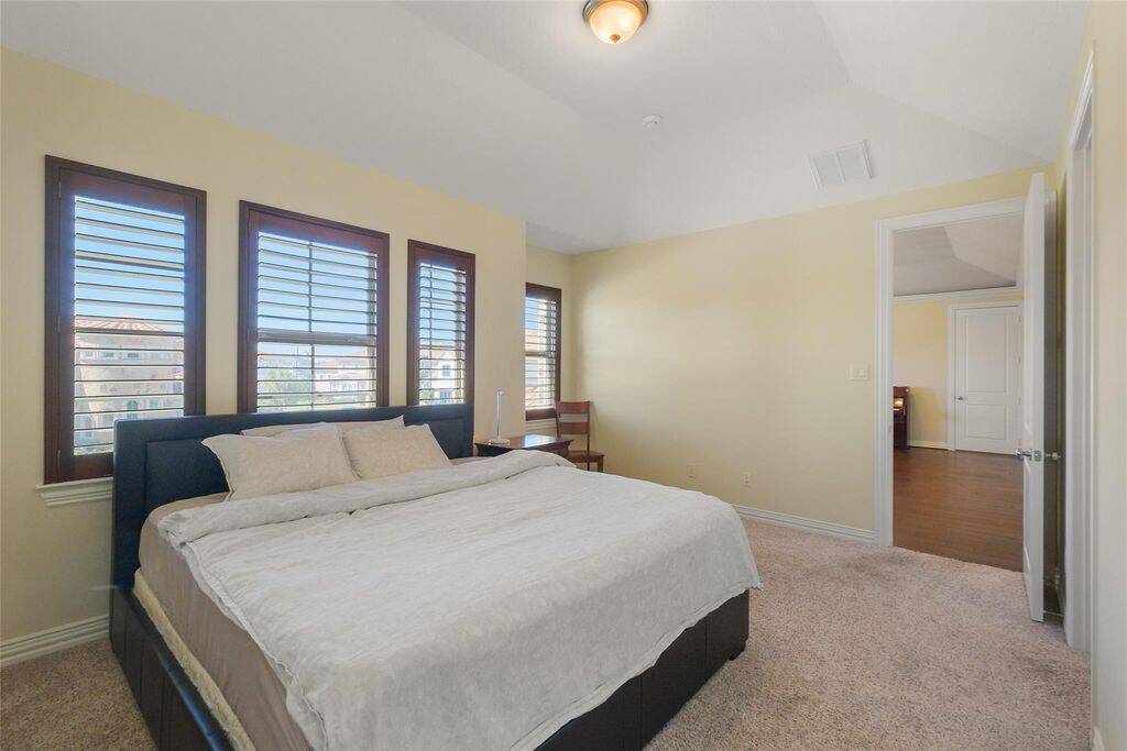 This inviting upstairs bedroom offers a serene retreat with vaulted ceilings, plush carpeting, and abundant natural light. Three large windows with elegant wooden shutters provide a picturesque view of the surrounding neighborhood while ensuring privacy and light control.The spacious layout comfortably accommodates a king-sized bed and additional furnishings, making it a perfect guest room or family bedroom.