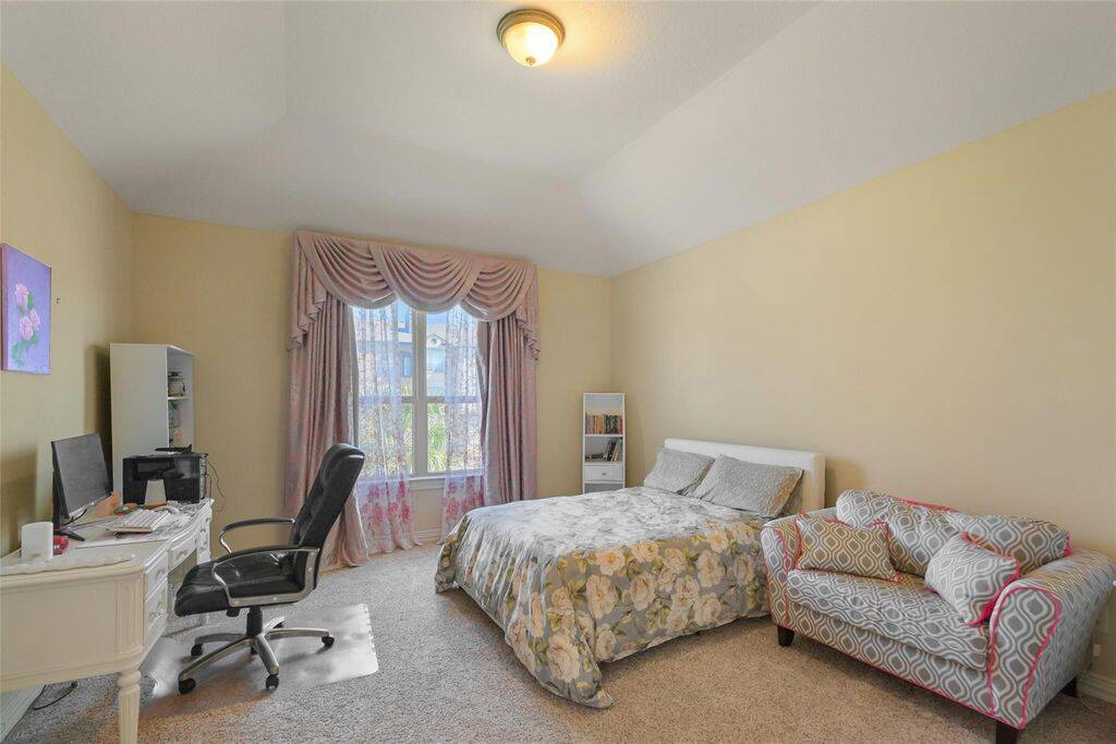 This expansive bedroom offers a perfect blend of comfort and sophistication. The vaulted ceiling enhances the sense of space, while the large window with elegant drapes allows natural light to fill the room, creating a warm and inviting ambiance.