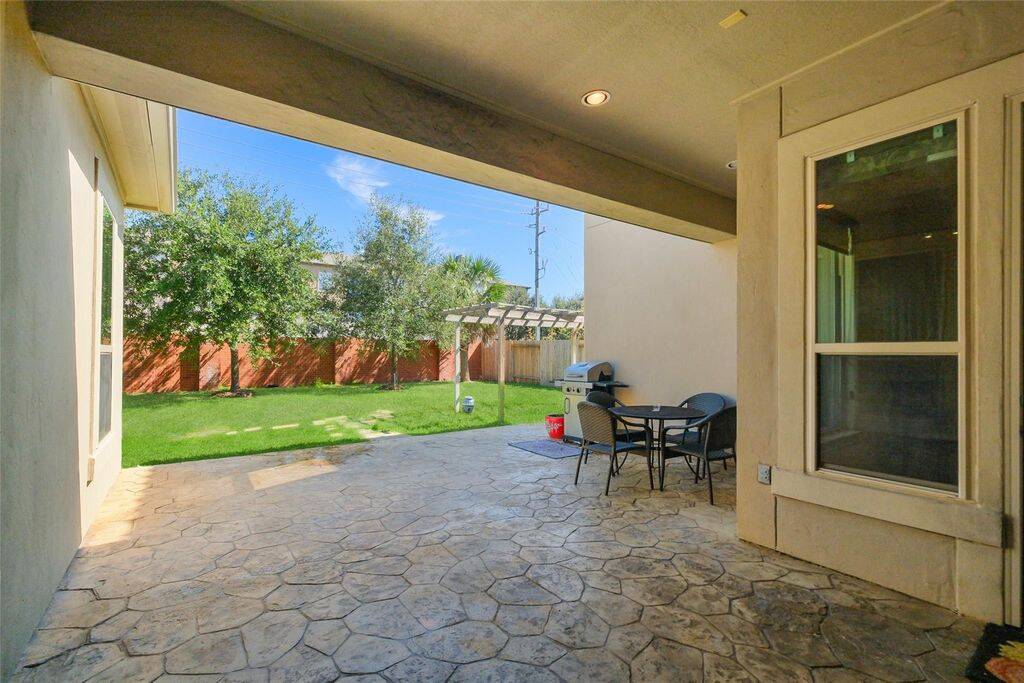 This photo showcases a cozy patio area with stone flooring, perfect for outdoor dining and relaxation. It opens to a lush green backyard with privacy fencing, ideal for entertaining or enjoying quiet time.