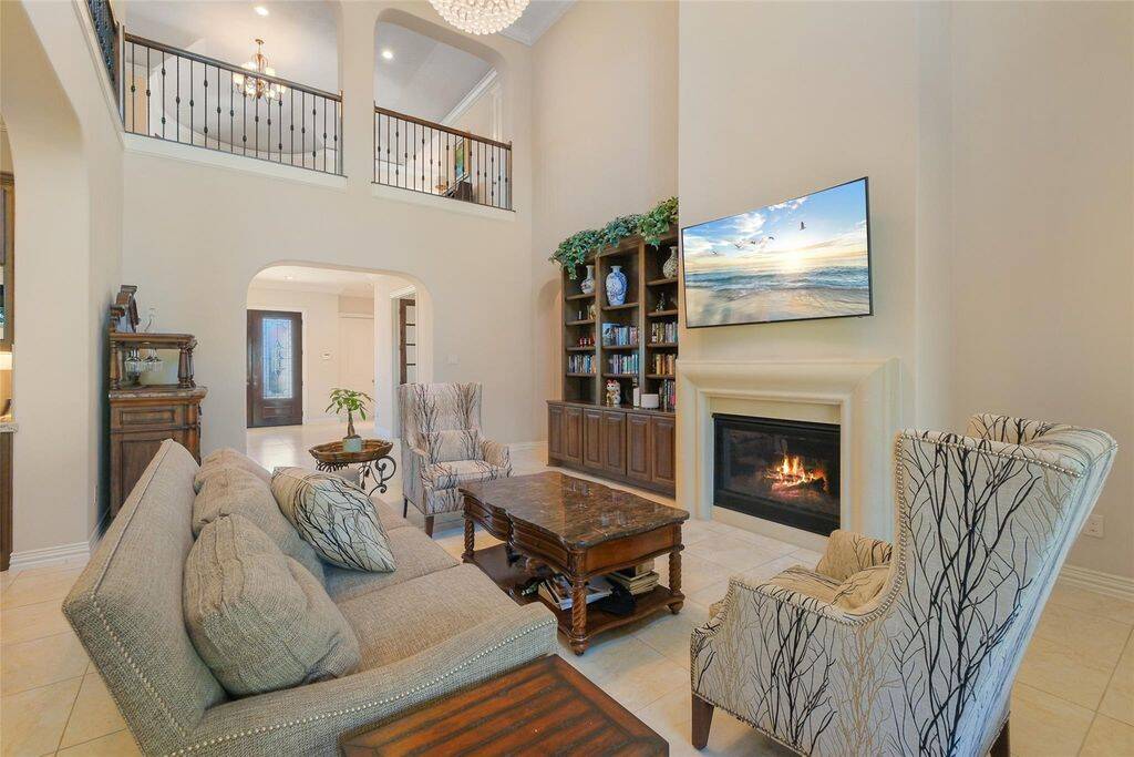 Soaring ceilings, a grand open loft, and a cozy fireplace set the stage for this breathtaking living space. Bathed in natural light from oversized windows, this two-story living room offers an airy, sophisticated atmosphere perfect for relaxation and entertaining. The elegant wrought iron railing adds a touch of grandeur, complementing the seamless flow of the open-concept design.