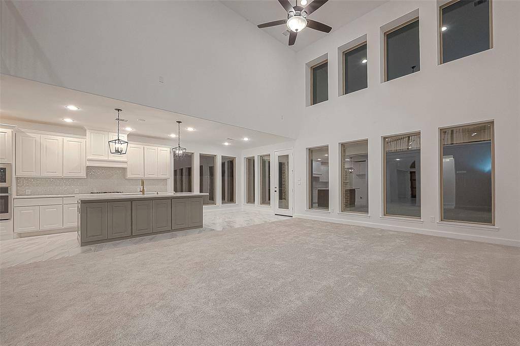 The spacious kitchen is a chef's dream, equipped with an oversized island boasting under-counter cabinets, quartz countertops, an under-mount sink, and 42-inch cabinets. Tile backsplash, a gas cooktop with hood, and built-in stainless-steel appliances further enhance the kitchen's functionality.