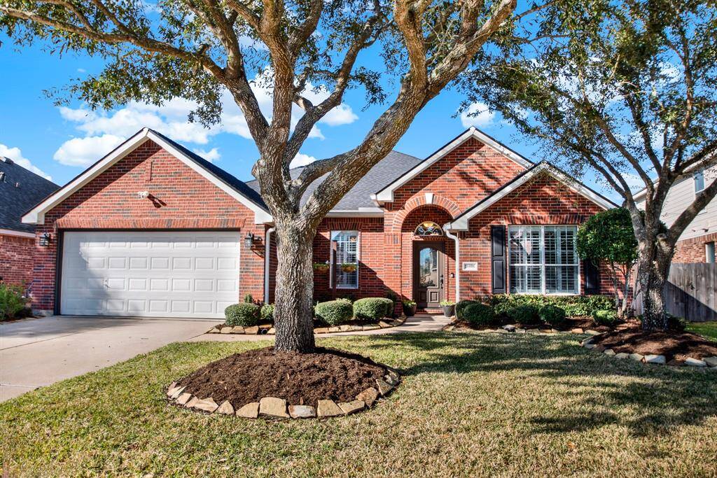 Charming red-brick home with a two-car garage and a well-maintained landscape with mature trees.